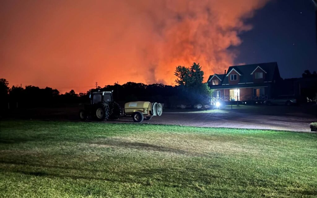 tractor	Orange glow and smoke from a nearby fire visible behind Jester Hill Wines at night, with the vineyard tractor in the foreground.